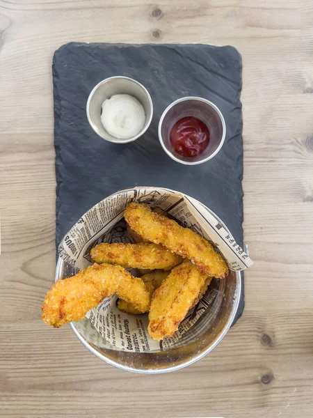 top view of a chicken fingers topping on a slate plate and two jars with barbecue sauce and mayonnaise, selective focus on fingers, vertical