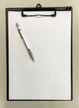 Gri bir masa üzerinde boş bir kağıt ve metal mekanik kalemle siyah bir pano klasörünün üst görünümü, kopyalama alanı, dikey