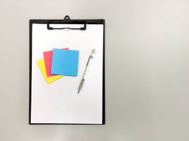 Boş bir kağıt, metal mekanik bir kalem ve gri bir masa üzerinde çok renkli bir not kağıdı olan siyah bir dosya klasörünün üst görünümü, kopyalama alanı, yatay