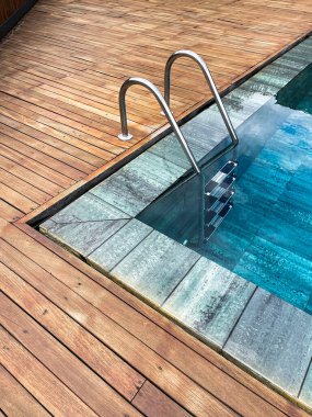 Bir kaplıcanın kenarsız havuzunda merdiven ayrıntıları, dış tarafı meşe ağacıyla çevrili, derin mavi kristal berrak su, dikey