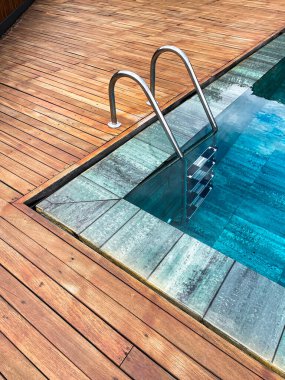 Bir kaplıcanın kenarsız havuzunda merdiven ayrıntıları, dış tarafı meşe ağacıyla çevrili, derin mavi kristal berrak su, dikey