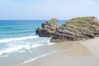 İspanya 'nın Las Catedrales Sahili' nde el değmemiş, kumları süpüren iki deniz yığınının yüksek açılı görüntüsü. Sakin mavi sular ve dalgalı beyaz dalgalar manzaralı kıyı manzarasını tamamlıyor.