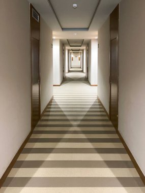 Çizgili halı, ahşap kapılar ve simetrik ışıklandırma olan uzun ve modern bir otel koridorunun iç görünümü. Minimalist mimari, dikey simetrik bileşim