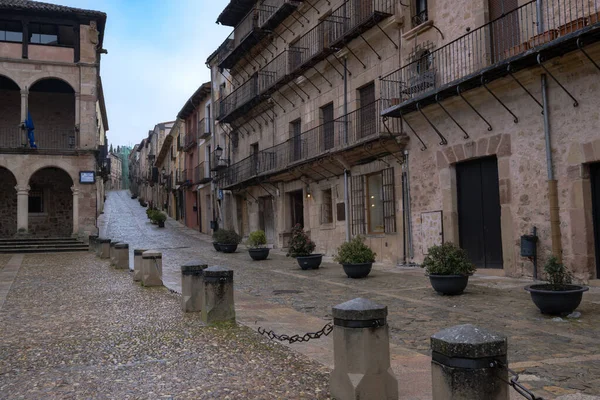 Siguenza, Guadalajara, İspanya 'da eğimli bir kaldırım taşı caddesinde geleneksel balkonları olan tarihi taş binalar, yumuşak bir kış gökyüzü altında ortaçağ mimarisi ve kırsal şehir cazibesine sahip.