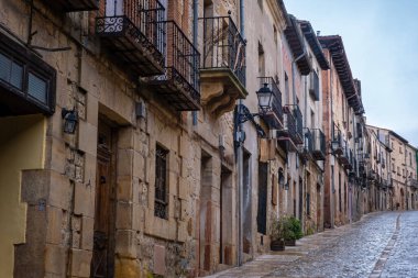 Siguenza İspanya 'nın tarihi kaldırım taşı caddesinde ortaçağ İspanyol köyünde günışığı altında süslü demir balkonları ve klasik sokak lambaları olan geleneksel taş evler var.