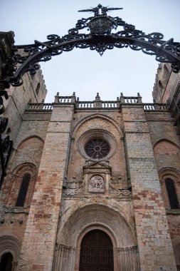 Roma cephesinin alçak açısı ve Siguenza Katedrali 'nin kuleleri etkileyici bir gökyüzü altında, Guadalajara, İspanya' daki tarihi ortaçağ taş mimarisi, işlenmiş demirden bir kemer vasıtasıyla,