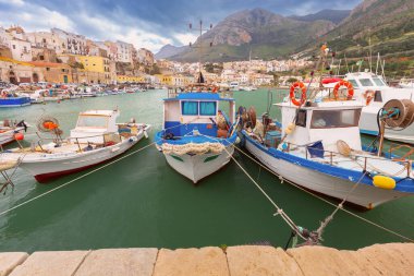 Balıkçı tekneleri, arkasında dağlar ve binalar olan küçük bir limana demirledi. Sicilya, İtalya..
