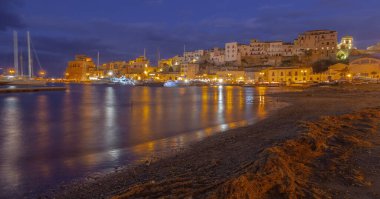 Sicilya 'daki Castellammare del Golfo' nun akşam manzarası. Limanda aydınlatılmış rıhtım binaları ve tekneleri var.