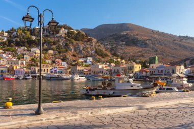 Yunanistan 'ın Symi kıyısında kıyıya vuran küçük tekneler yamaç kenarındaki evler ve günbatımında sakin denizler