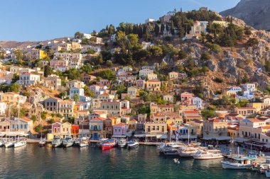 Güneşli gökyüzünün altında Pastel neoklasik evler ve kayalık tepeler ile birlikte Suriye adasının sakin limanına demirlemiş küçük balıkçı tekneleri.