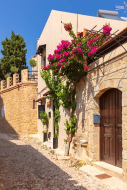 Yunanistan 'ın Rodos antik kentinde kaldırımları, çiçekli begonvilleri olan sessiz dar bir ara sokak.