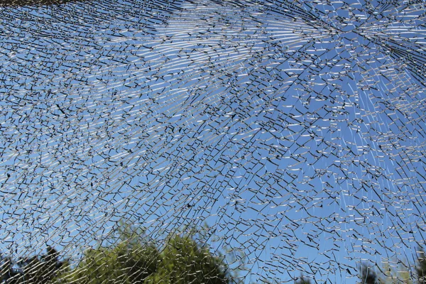 Una ventana de vidrio de puerta corredera se rompió en un millón de piezas con un cielo azul detrás de ella . — Foto de Stock