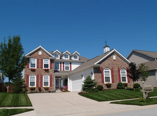 Two story brick residential home with red shutters, window flower boxes and weather vane with plenty of copy space. — Stock Photo, Image