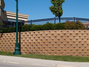 Large retaining wall with a black wrought iron fence behind bushes running along the top. clipart
