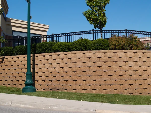 Large retaining wall with a black wrought iron fence behind bushes running along the top.