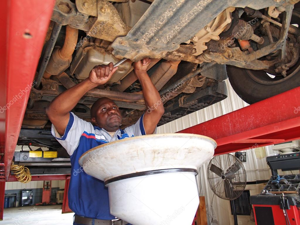 Auto mechanic performing an oil change with the car on a lift in a
