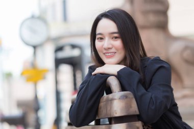 Siyah uzun kollu gömlekli Asyalı güzel bir kadın parktaki sandalyede oturuyor..