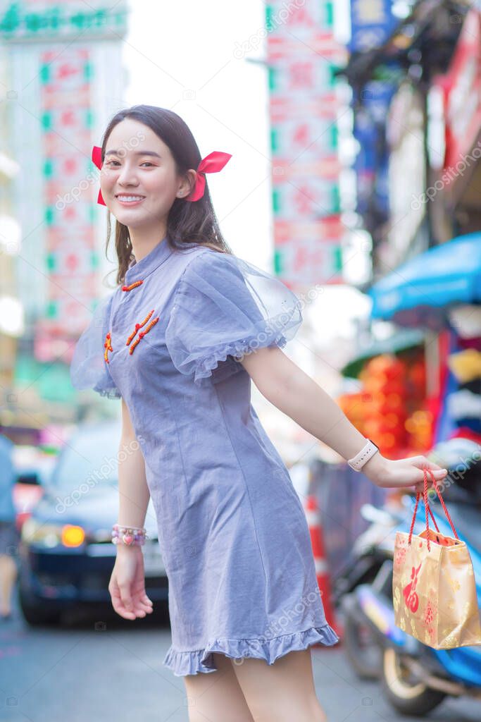 Asian beautiful woman in Chinese dress is smiling and walking on street in China town, Thailand.