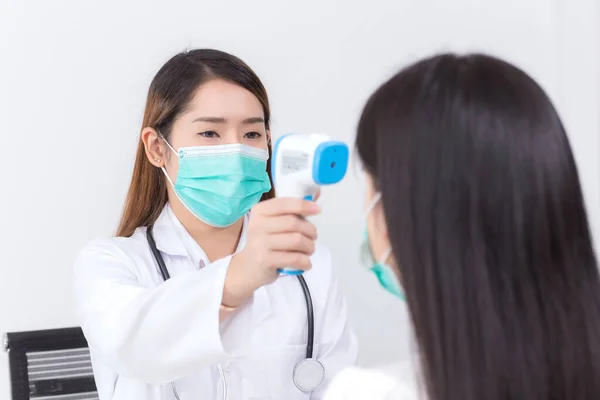 アジアの女性医師は 患者の体温を測定するために赤外線額温度計を使用し それらの両方が健康管理の概念でコロナウイルス Covid を保護するために医療面マスクを着用します — ストック写真