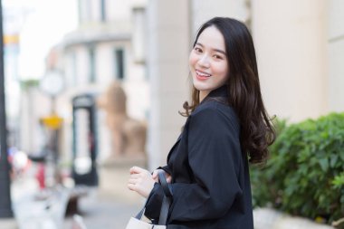 Güzel, uzun saçlı, siyah paltolu bir Asyalı kadının portresi. Şehirde yürüyor ve gülümsüyor..