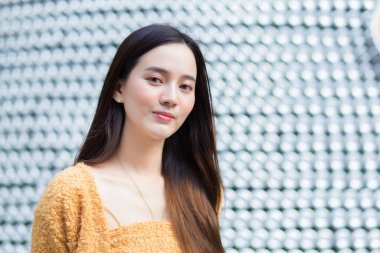 Uzun saçlı Asyalı güzel bir kadın sarı bir kazak giyiyor ve parlak bir şekilde gülümsüyor. soyut arkaplan.