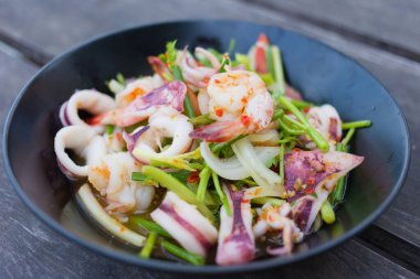 Karides ve kalamarlı baharatlı salata ile doğranmış domates ve soğan siyah tabakta karıştırıldı..