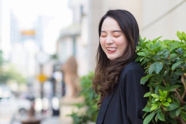 Asyalı güzel, uzun saçlı, siyah paltolu kadın şehirde mutlu bir şekilde dikiliyor..