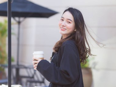 Koyu mavi takım elbiseli Asyalı güzel kadın mutlu bir şekilde gülümsüyor. Güneşli bir sabahta kahve dükkanının önünde.