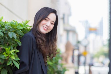 Uzun saçlı, siyah ceketli, güzel bir Asyalı kadının portresi. Kentte mutlu bir şekilde gülümsüyor.