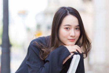 Koyu mavi uzun kollu gömlekli Asyalı güzel bir kadın parktaki sandalyede oturuyor..