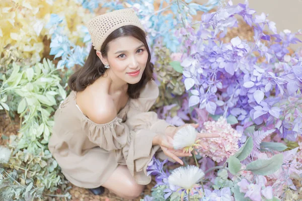 Asian beautiful woman in pretty dress is smiling while holds flower bouquet in her hands at flower garden