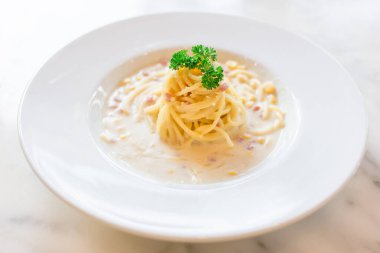 Jambon ve mısırla karıştırılmış beyaz krema soslu spagetti İtalyan restoranında beyaz bir tabakta servis ediliyor..