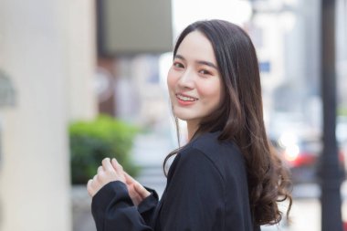 Güzel, uzun saçlı, siyah ceketli Asyalı bir kadının portresi ve açık havada gülümsemesi..