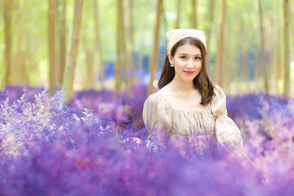 Asian beautiful woman who wears dress is sitting in purple flower garden and smiling happily.