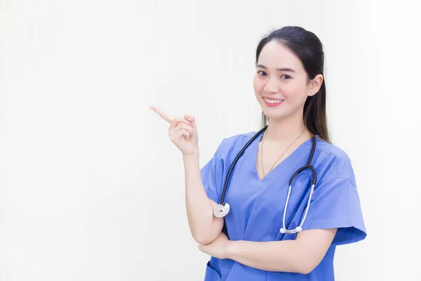 身穿蓝色制服的亚洲漂亮女医生站在那里笑着 同时指着白底的顶部 — 图库照片