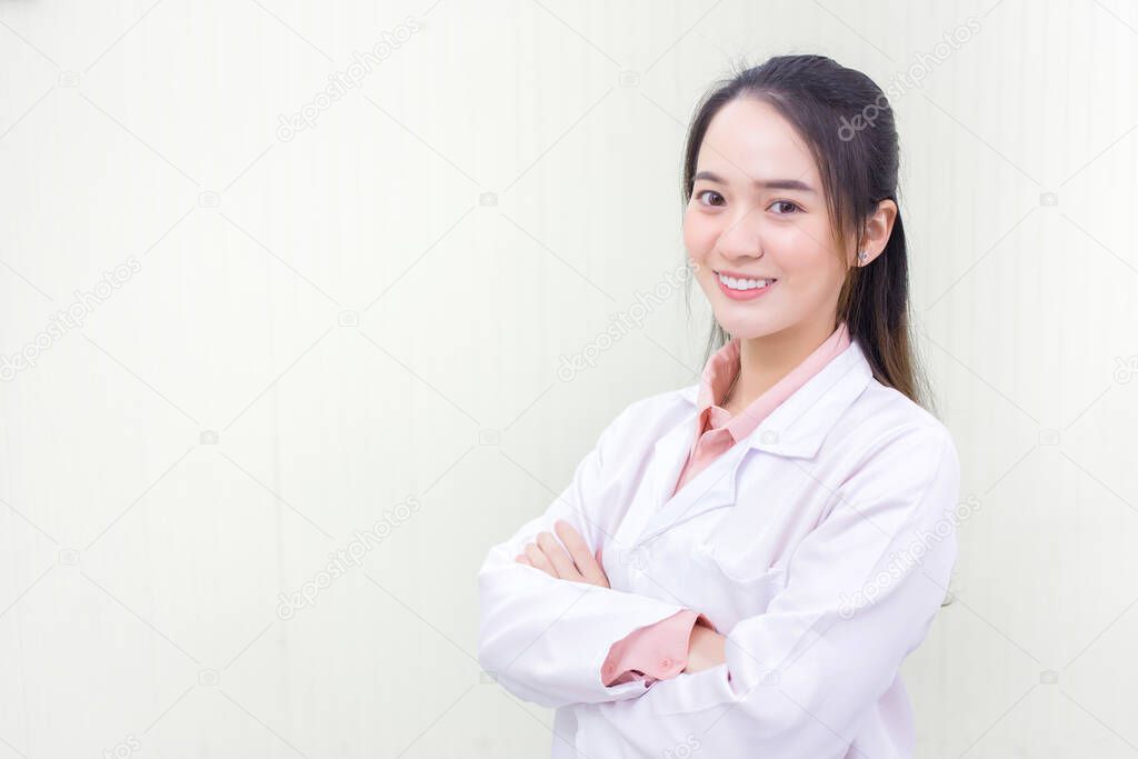 Asian woman doctor who she has a black long hair, wear a stethoscope and a white lab coat as a uniform while arm cross at office room in hospital in health care,new normal and coronavirus protection concept.