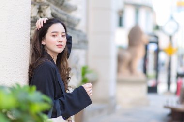 Koyu mavi cüppeli Asyalı uzun saçlı kadın dışarı bakıyor ve dışarıda duruyor. Kasabada bir şey bekliyor..