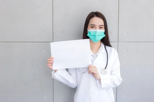 白い医療コートと顔のマスクを身に着けているアジアの女性医師は立ち コロナウイルスの医療概念に何かを言うために白い紙を示しています — ストック写真