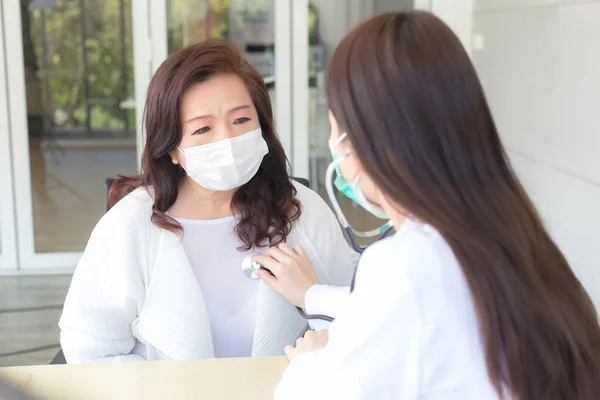 亚洲女医生使用听诊器检查病人的肺和心脏健康状况或诊断症状 同时两人都在医院配戴口罩和验尸保护概念 — 图库照片