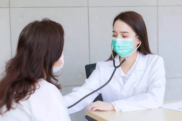 亚洲女医生使用听诊器检查病人的肺和心脏健康状况或诊断症状 同时两人都在医院配戴口罩和验尸保护概念 — 图库照片