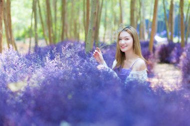 Asyalı güzel kadın, mor çiçek bahçesinde mutlu bir şekilde gülümsüyor..