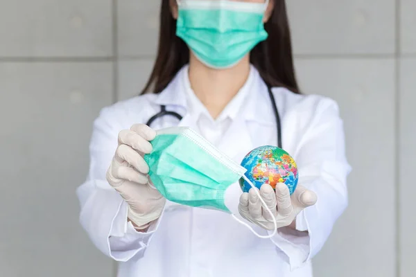 Asian woman doctor holds global ball and medical face mask as sign save world and new normal lifestyle theme.