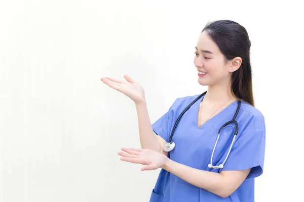 白い背景の上を指しながら青い制服を着たアジアのプロの女性医師が立って笑顔 — ストック写真
