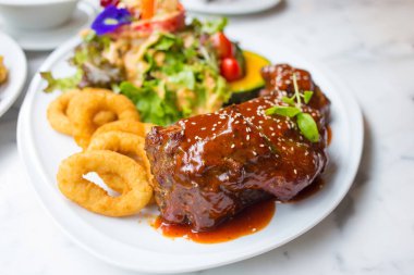 Izgara domuz pirzolası, barbekü sosu ve beyaz tabakta sebze.