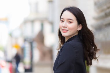 Uzun saçlı, güzel bir Asyalı kızın resmi. Siyah bornozlu güzel bir kız. Mutlulukla yürüyor ve dışarı bakıyor..