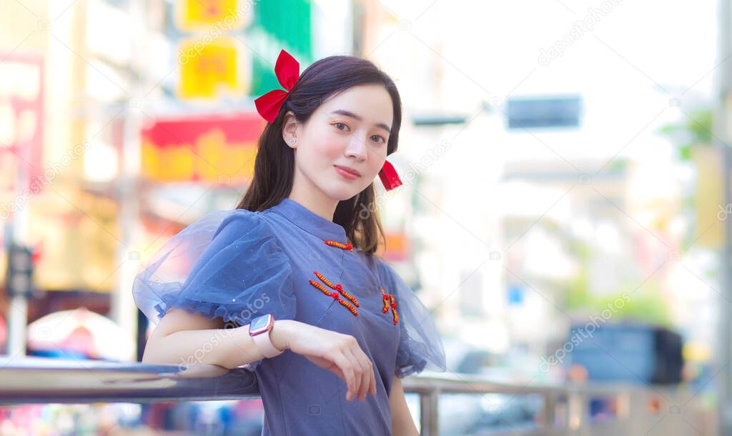 A beautiful Asian girl in blue-grey Qipao dress is standing smiling happily. Roadside China Town, Thailand Chinese New Year theme.