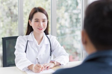 Tıbbi önlük giyen Asyalı profesyonel kadın doktor bir hastayla konuşup ona sağlık hizmetleri hakkında bilgi veriyor..