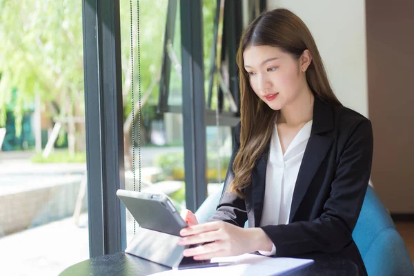 Asian professional  working woman in a black suit is working on an tablet on the table smiling happily in the office and working at home.