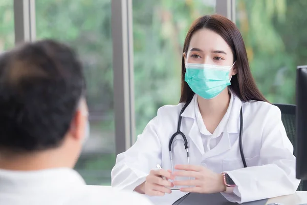 Asian elderly man patient consults with professional woman doctor about his symptom while doctor gives healthcare information with him at hospital.