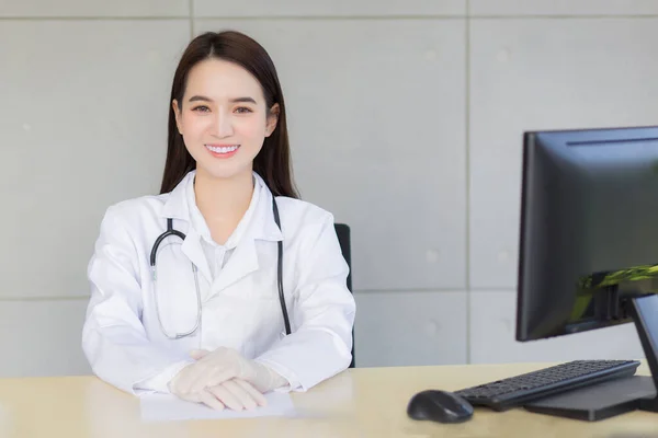 亚洲职业化年轻微笑的女医生坐在医院的办公室里 桌上有一张纸和一台电脑 — 图库照片